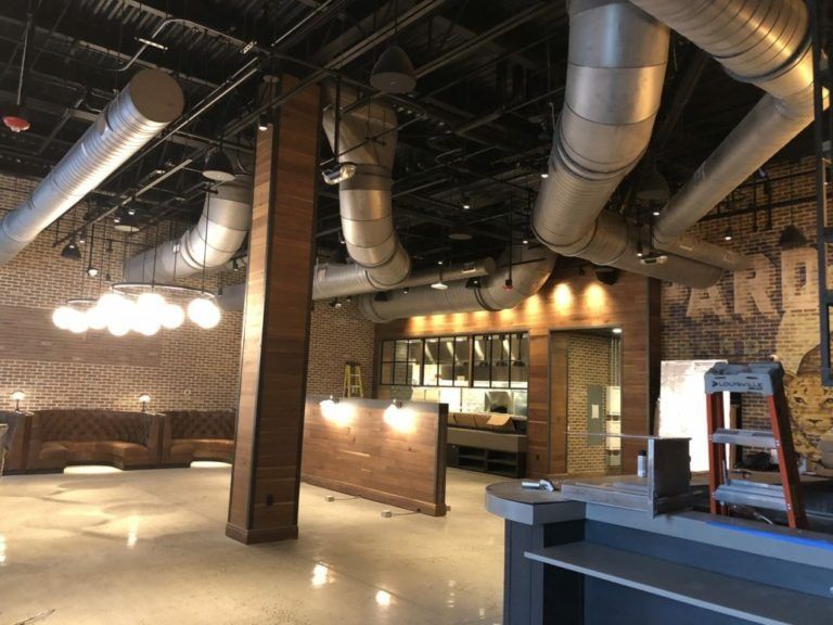Empty restaurant interior with exposed ventilation, brick walls, and a bar.