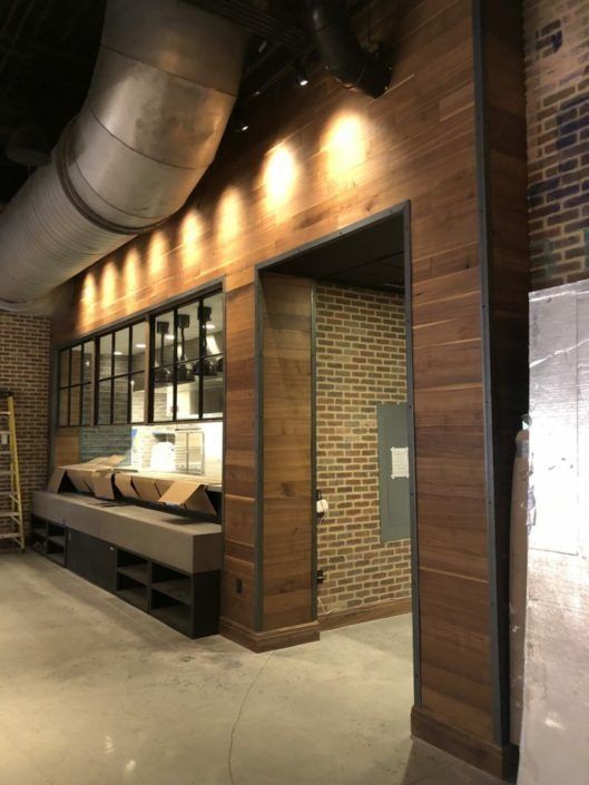 Interior with wood paneling, exposed brick, and a metal-framed doorway leading to another brick room; metal ventilation duct.