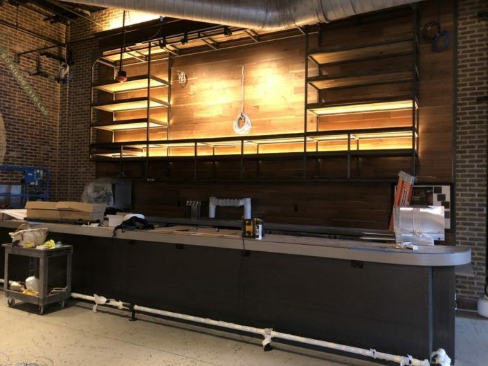 Bar area under construction with wooden shelving, a counter, and brick walls.