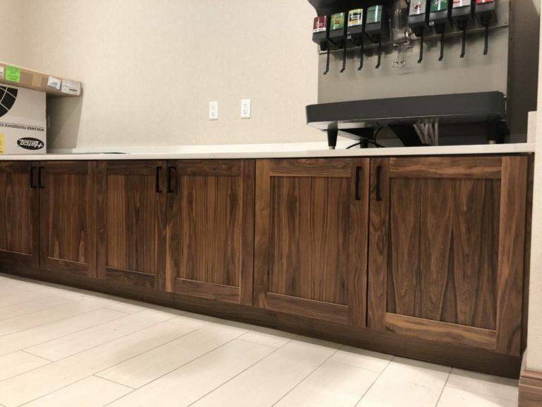 Wooden cabinets with dark handles below a soda fountain against a white countertop.