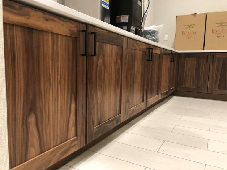 Wooden cabinets with black handles along a white countertop, and tiled floor.