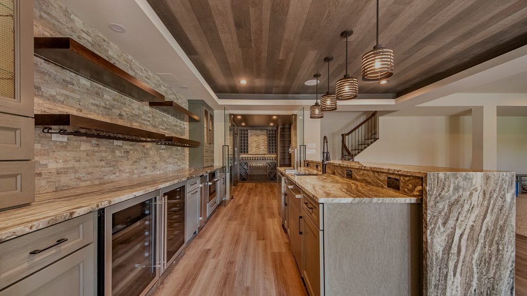 Basement bar with stone backsplash, wood shelves, wine coolers, and a long countertop.