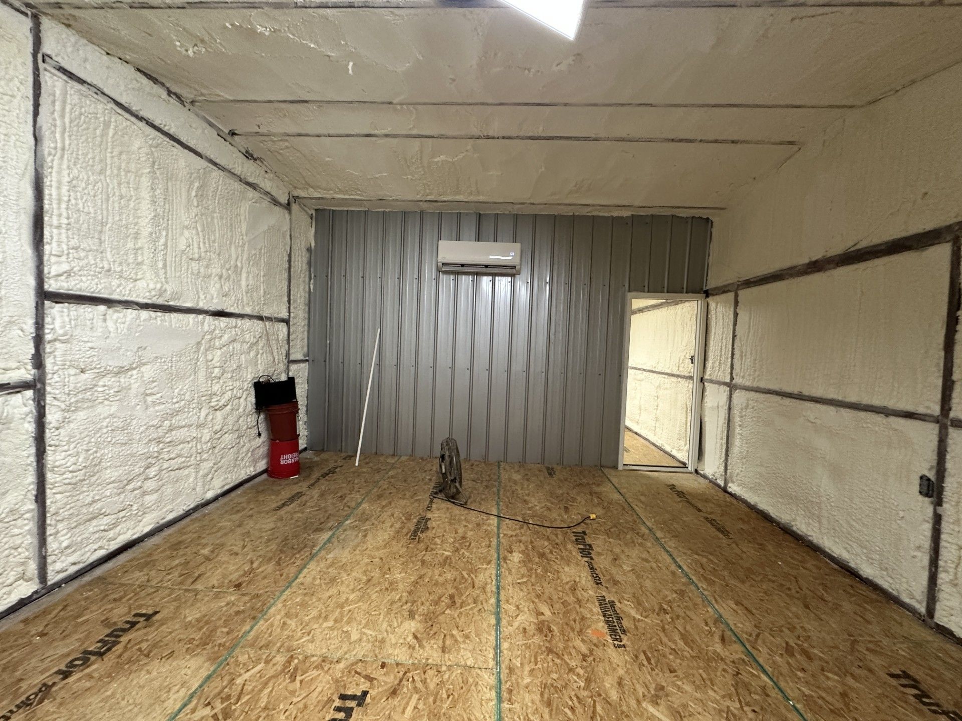 Empty indoor shooting lane with wooden floor, gray metal backstop, and a red fire extinguisher on the left.