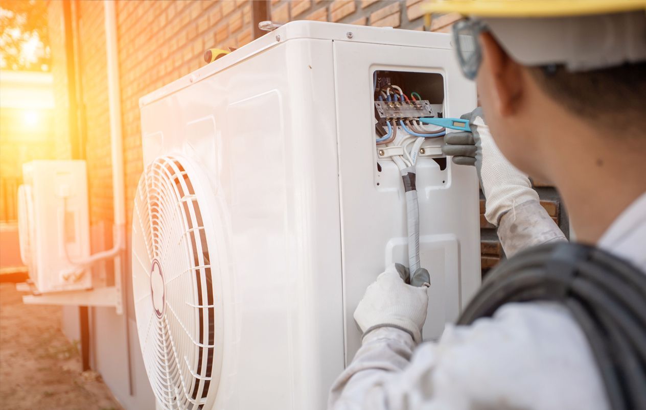 Technician inspecting wiring in an outdoor air conditioning unit during sunset