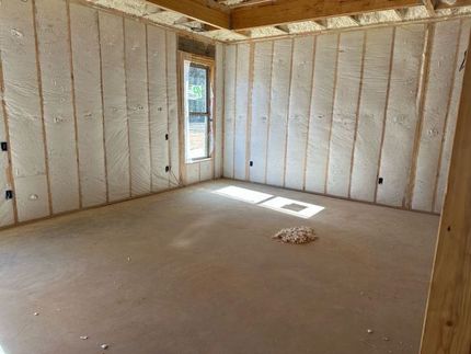 Interior of a room under construction, with insulated walls, wooden framing, and a window.