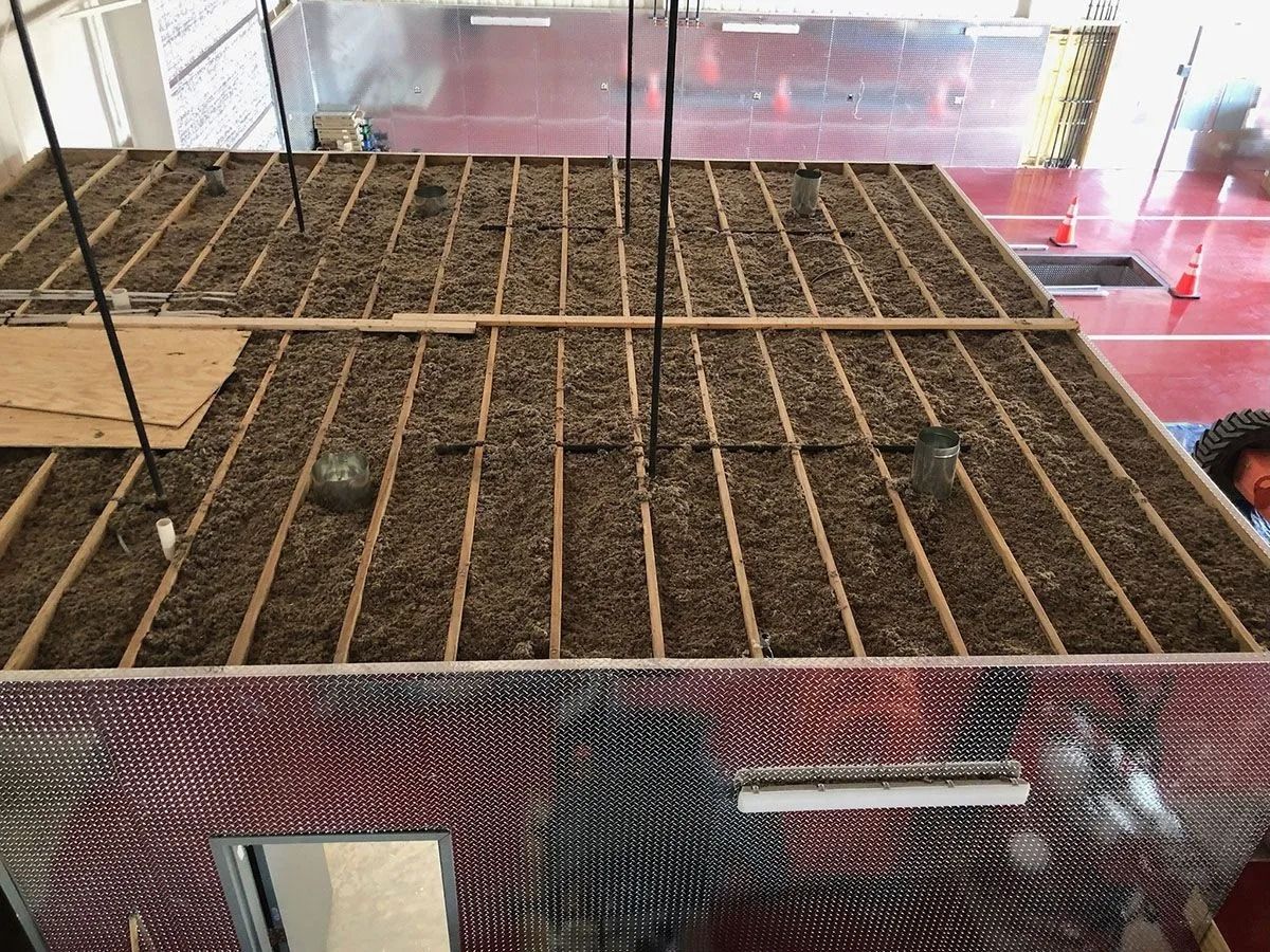 Overhead view of a rectangular structure with wooden beams filled with brown material, likely insulation. Shiny, silver walls.