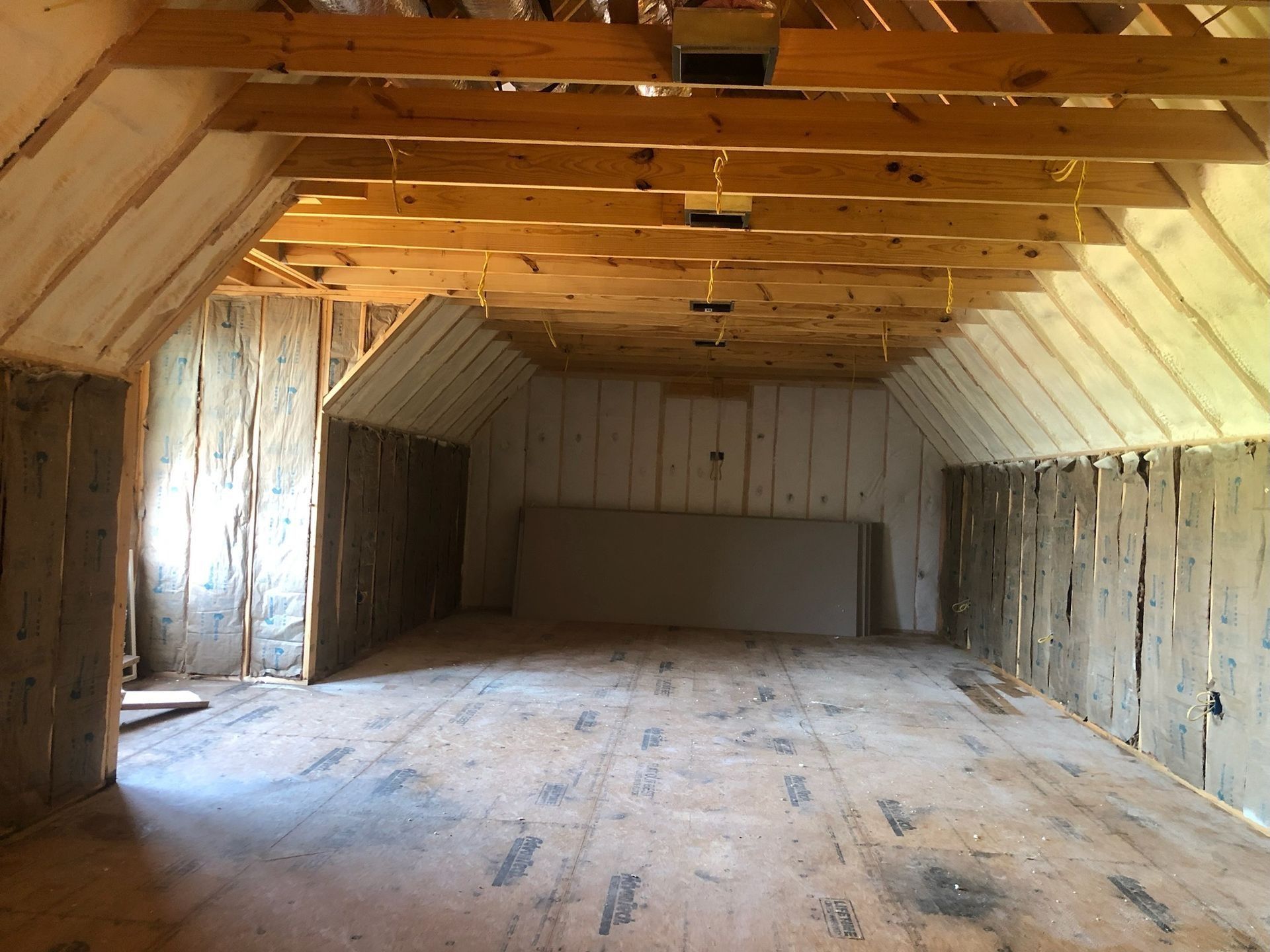 Interior of an attic under construction with exposed wooden beams, insulation, and unfinished walls.