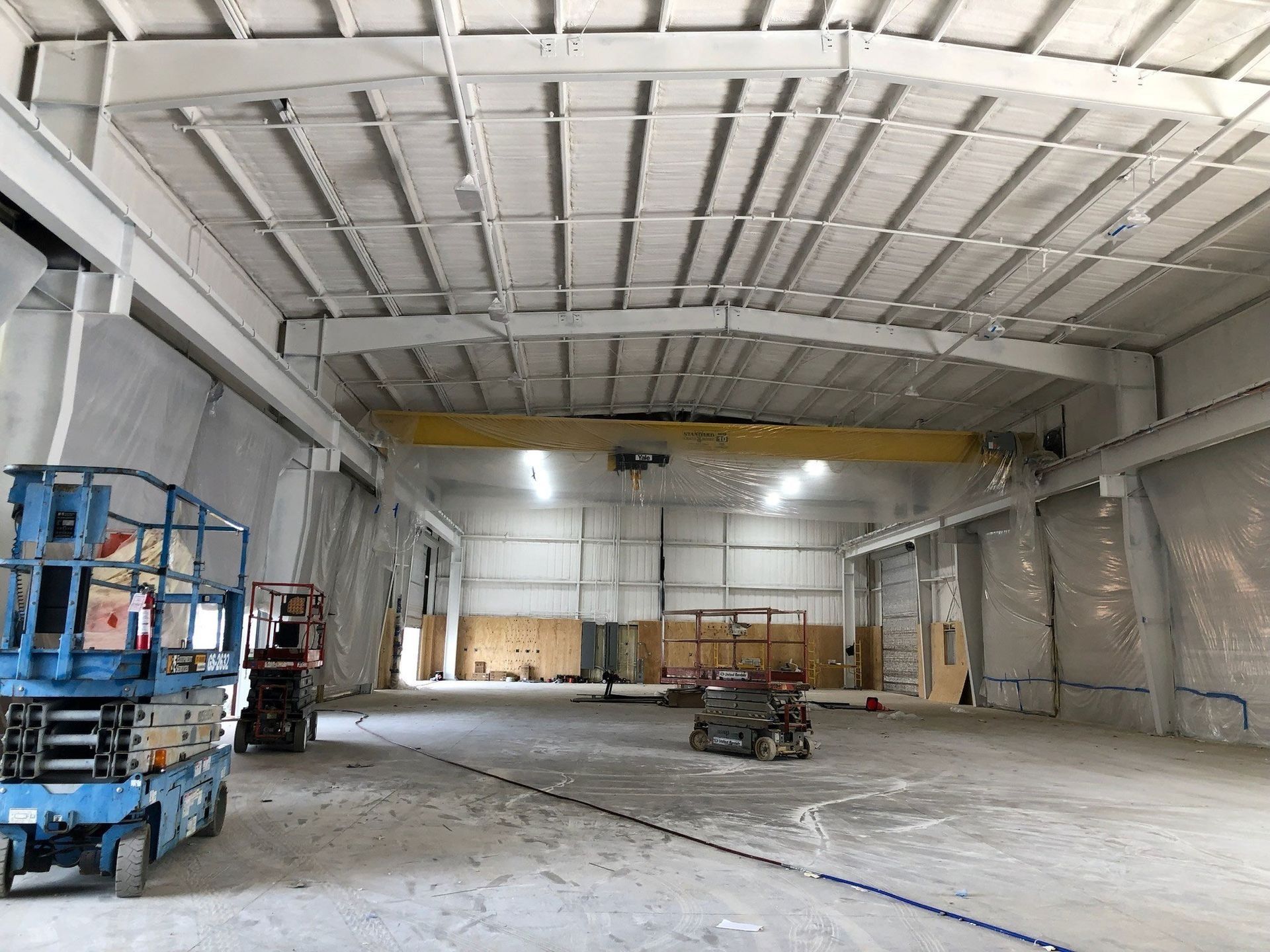 Large, empty industrial warehouse with high ceiling, metal beams, and a lift platform.