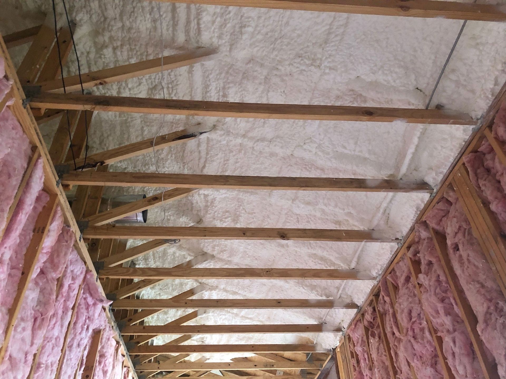 Interior view of a building's attic space. Spray foam insulation covers the rafters, and pink insulation lines the walls.