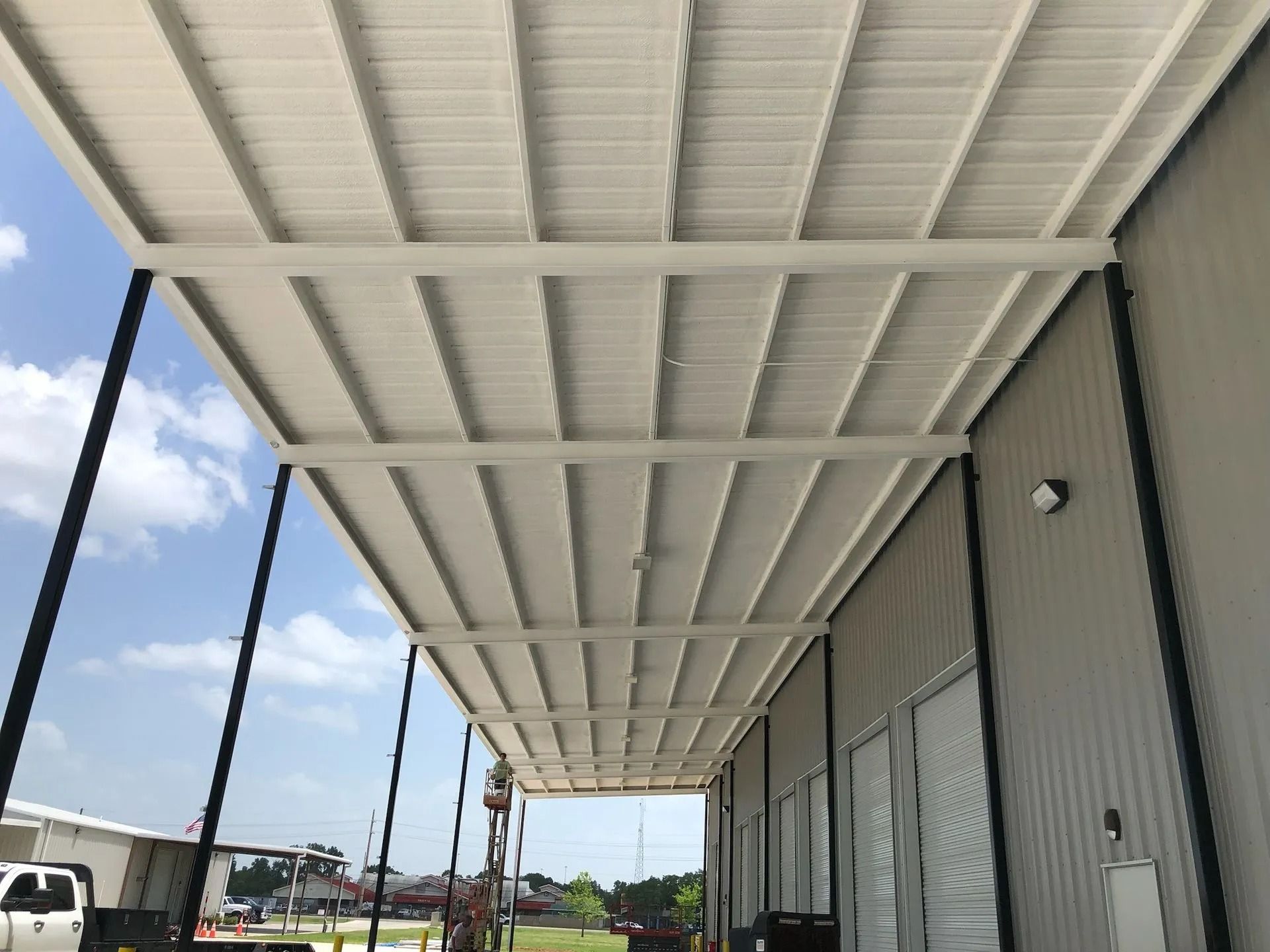 White metal awning over a building's side entrance, supported by black posts, against a blue sky.