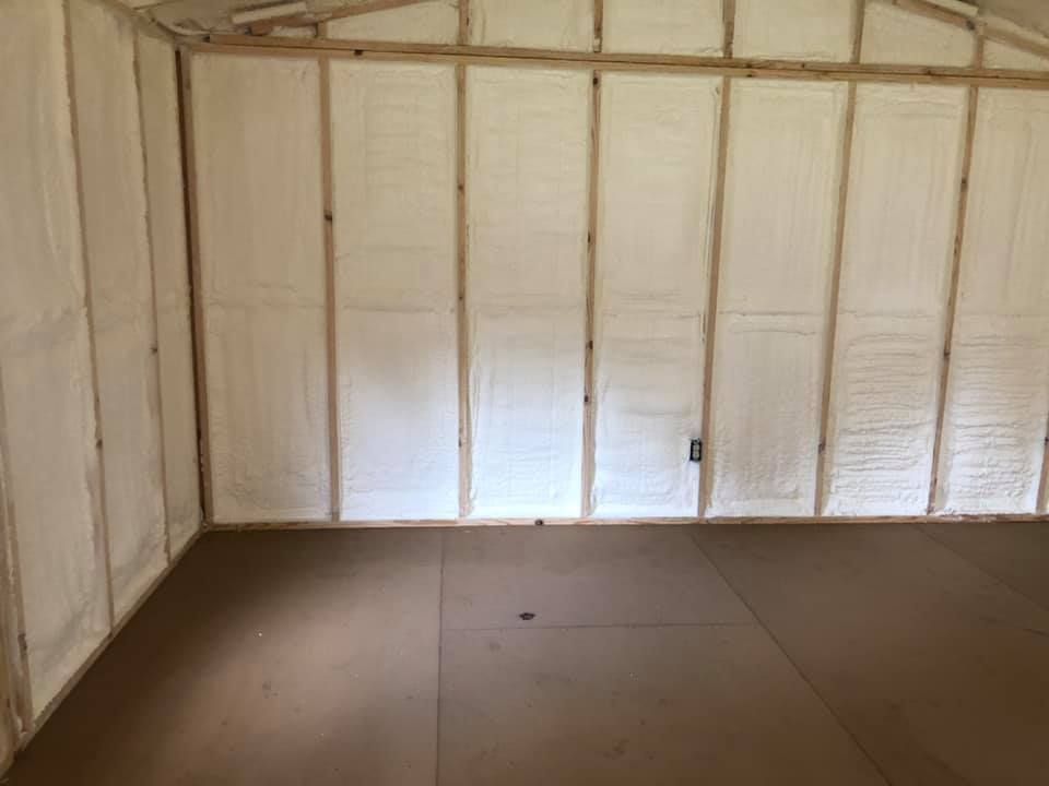 Interior of a room with spray foam insulation between wooden studs, and brown flooring.