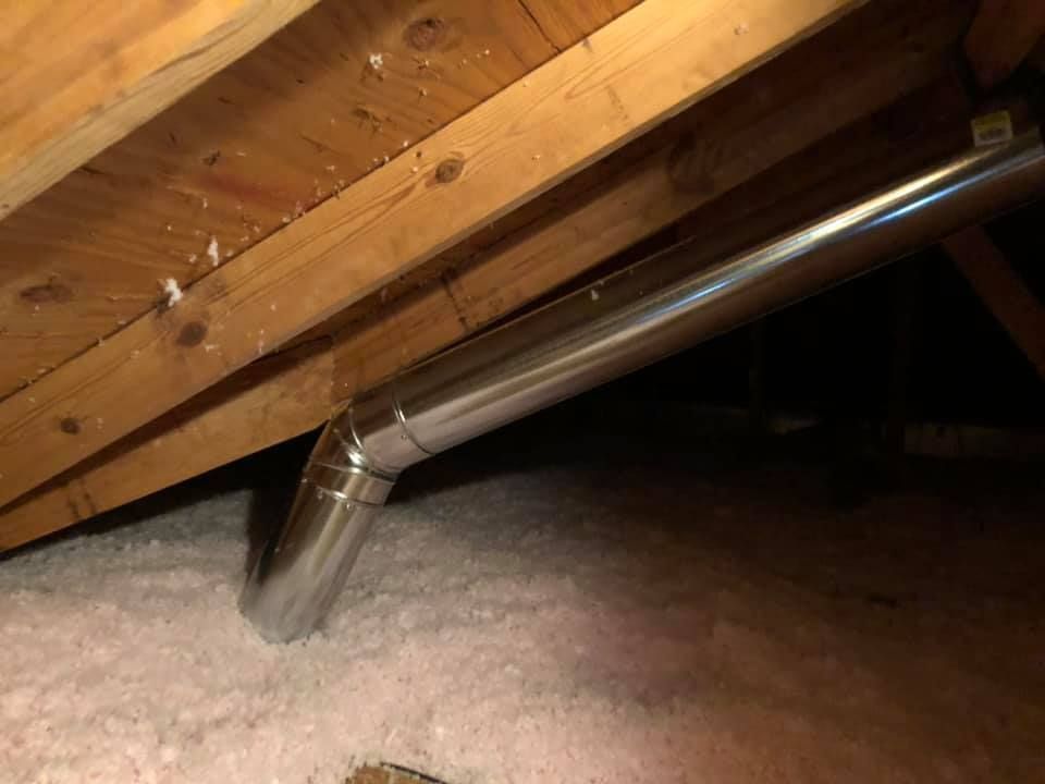 Metal ductwork passing through pink insulation in an attic, beneath wooden beams.
