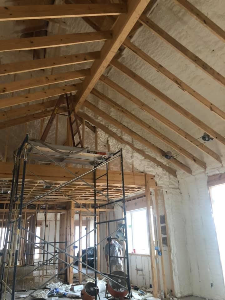 Interior view of a building under construction, showing wooden framing and spray foam insulation on walls and ceiling.