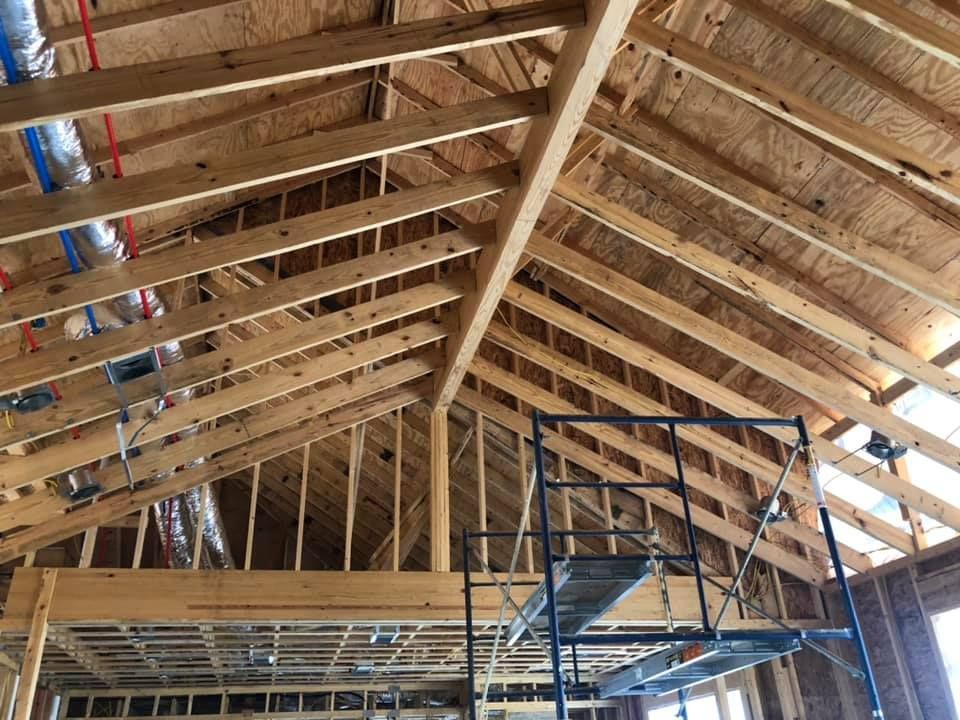 Wooden framework of a building's roof under construction. Scaffolding visible. Red and blue pipes.