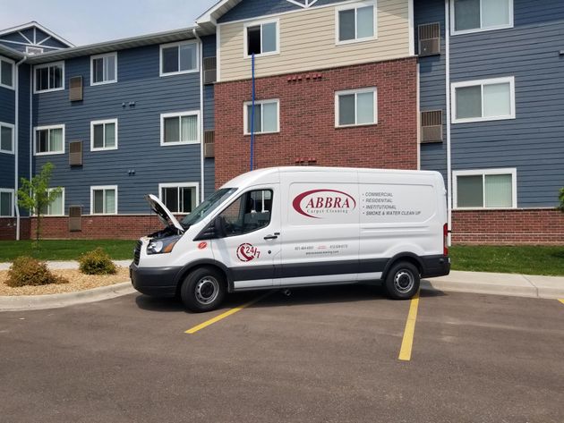 White service van parked in front of a blue and red apartment building, in a lot with yellow lines