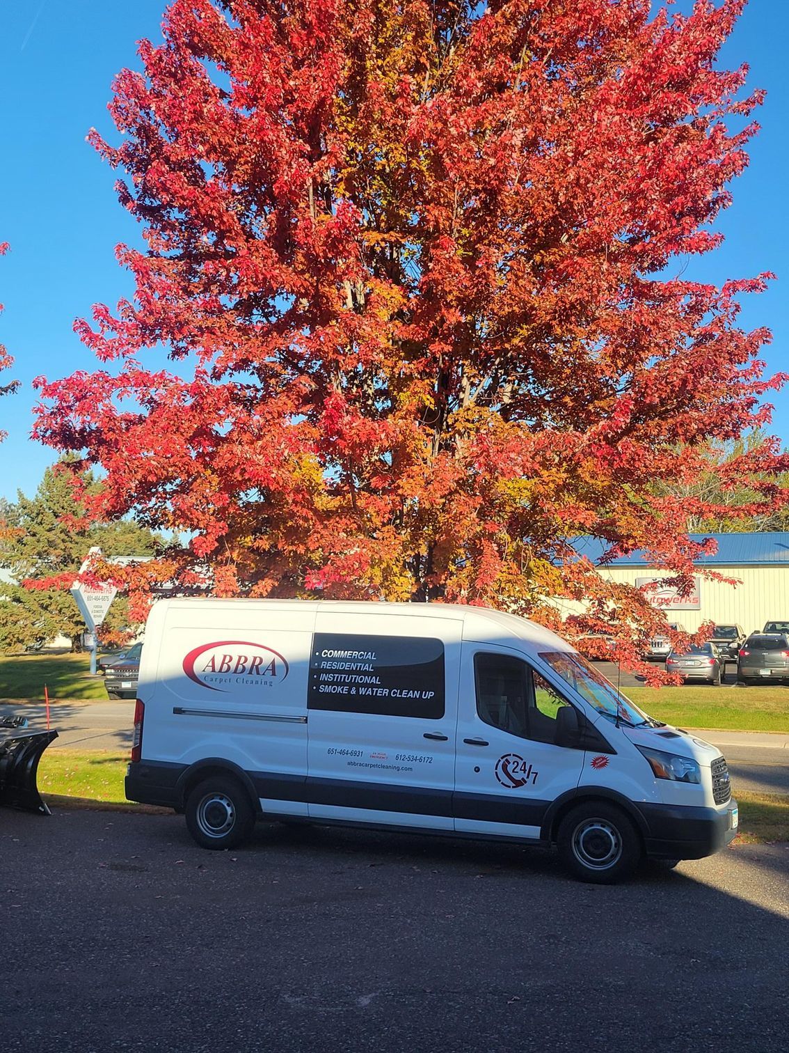 White service van parked under a яр red autumn tree on a sunny street