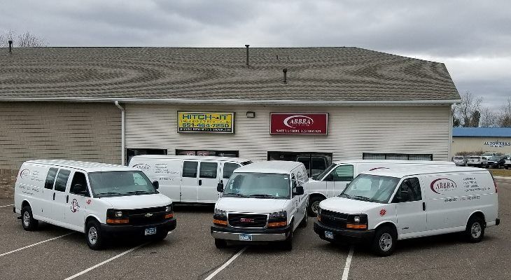 Three white cargo vans parked in front of a building with storefront signs.