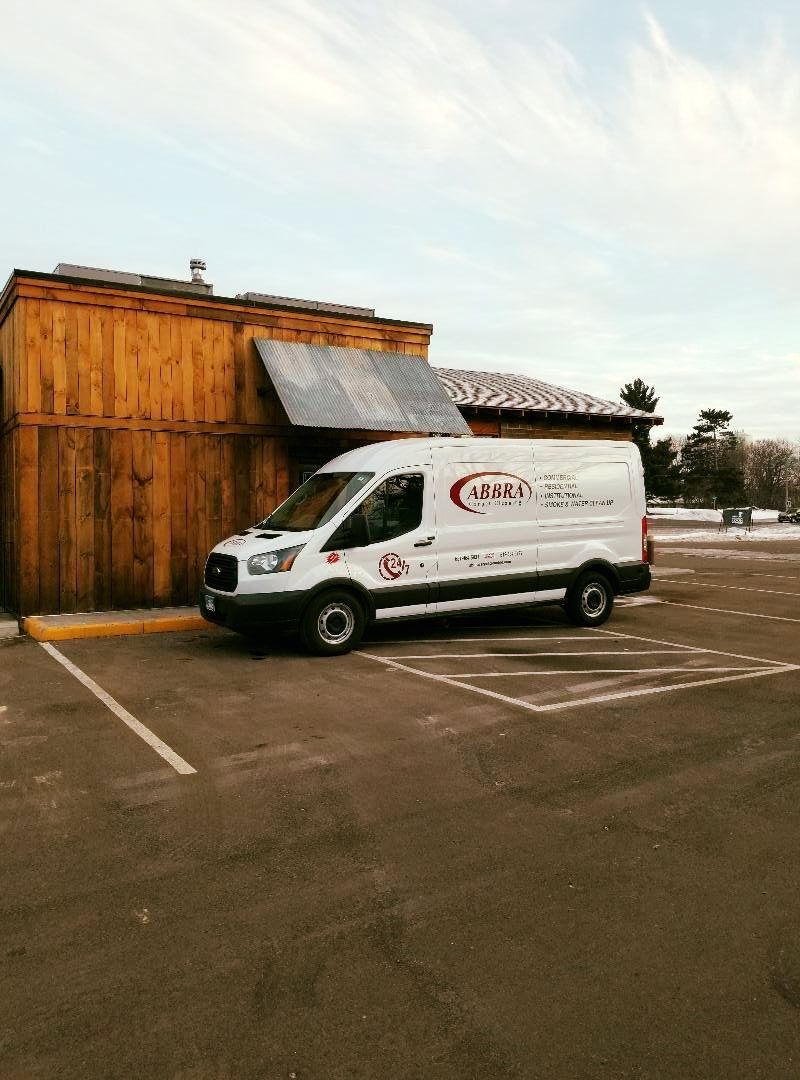 White service van parked beside a wooden building in an empty lot under a cloudy sky.