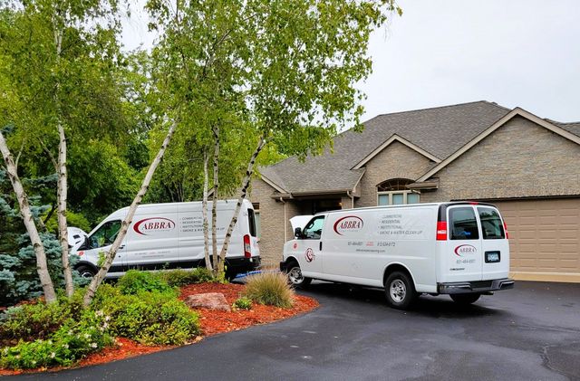 White service vans parked in a driveway beside a brick house and trees