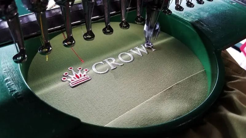 A machine is embroidery the word crown on a piece of fabric.