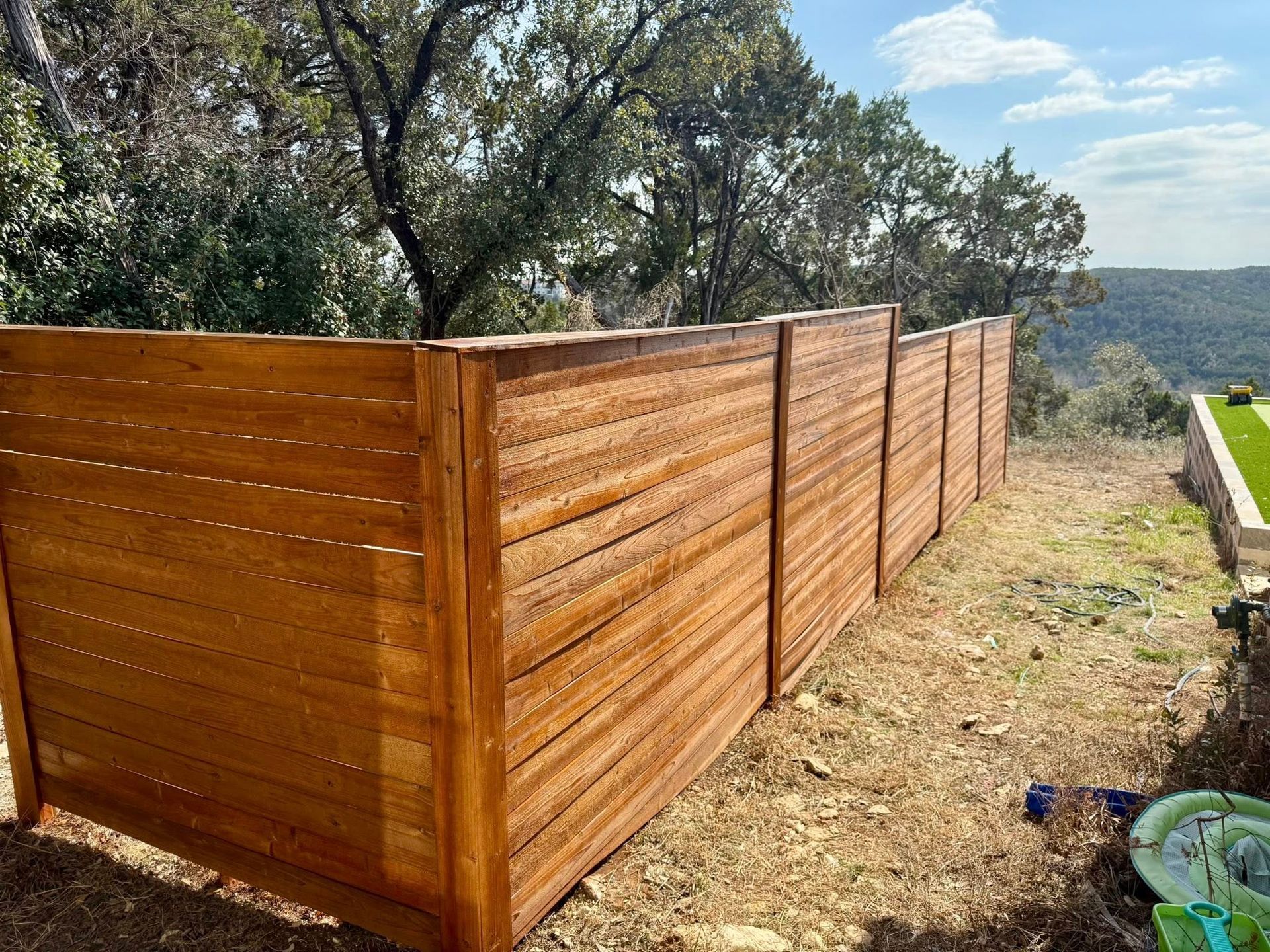 Wooden horizontal slat fence in a natural setting, brown wood, view of landscape.