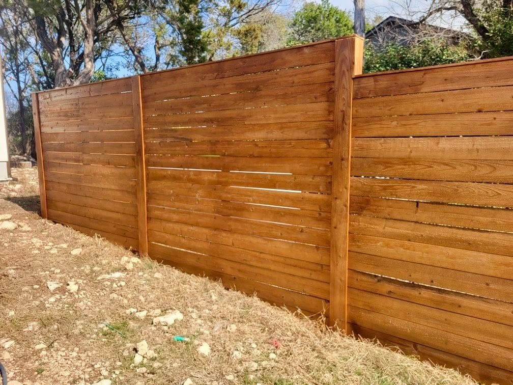 Wooden privacy fence, stained brown, on a grassy hill.