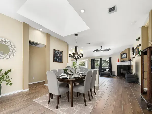 Dining room with table set for six, hardwood floors, chandelier, and a view of the living room with fireplace.
