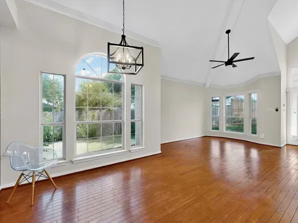 Empty room with hardwood floors, large windows, and a modern chair.
