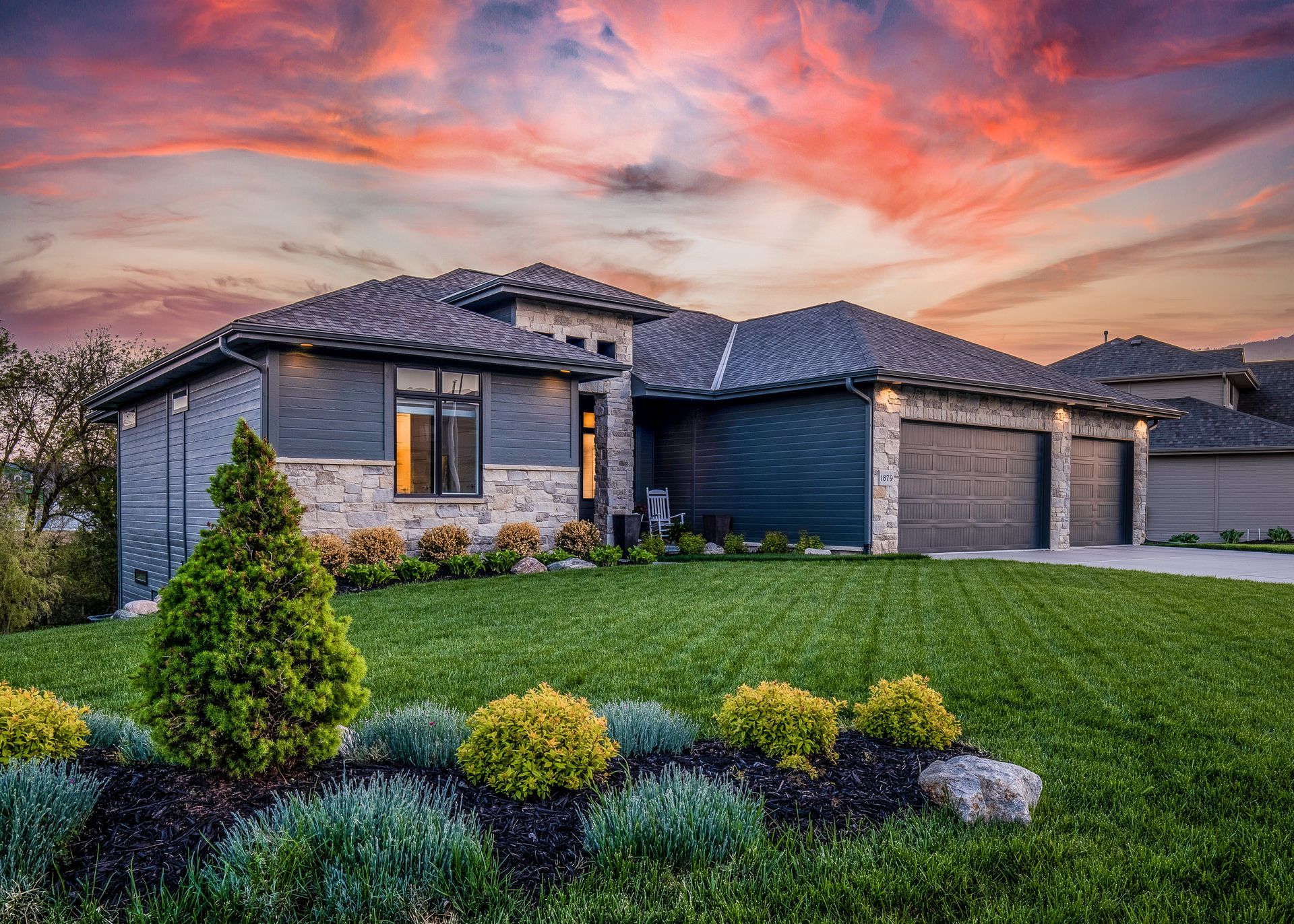 Modern house with stone and dark siding, manicured lawn, and sunset sky.