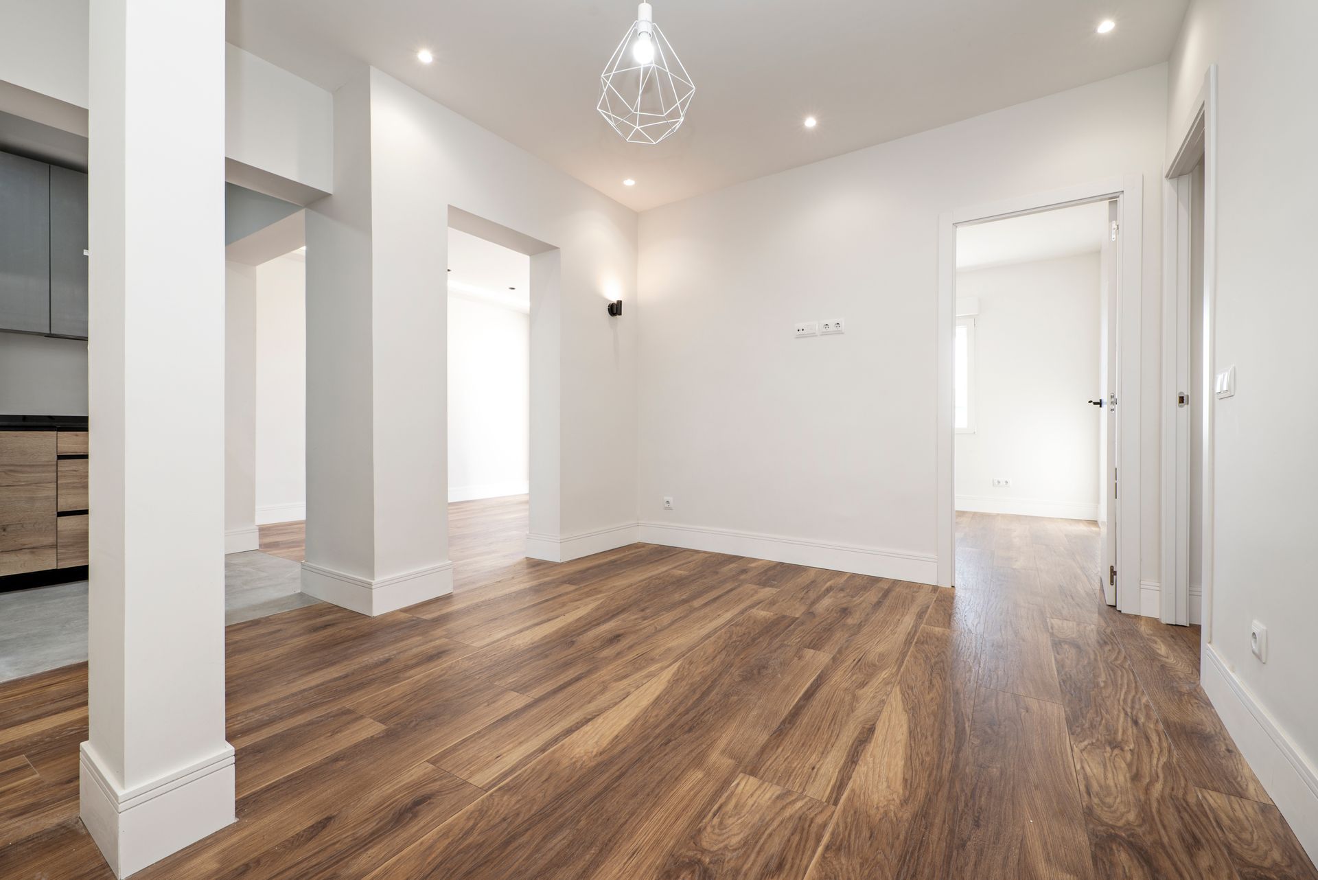 Empty, light-filled room with hardwood floors, white walls, and doorways leading to other rooms.
