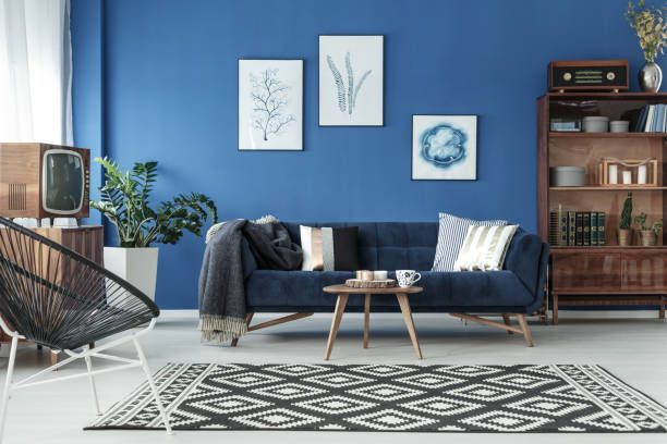 Blue living room with a sofa, patterned rug, wooden furniture, and framed art.