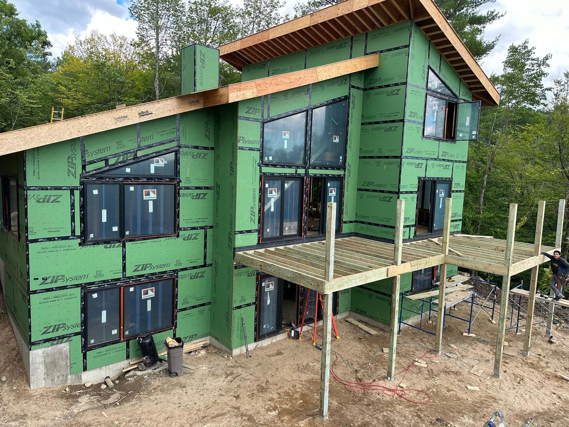 New house under construction, with green insulation, windows, and a deck.