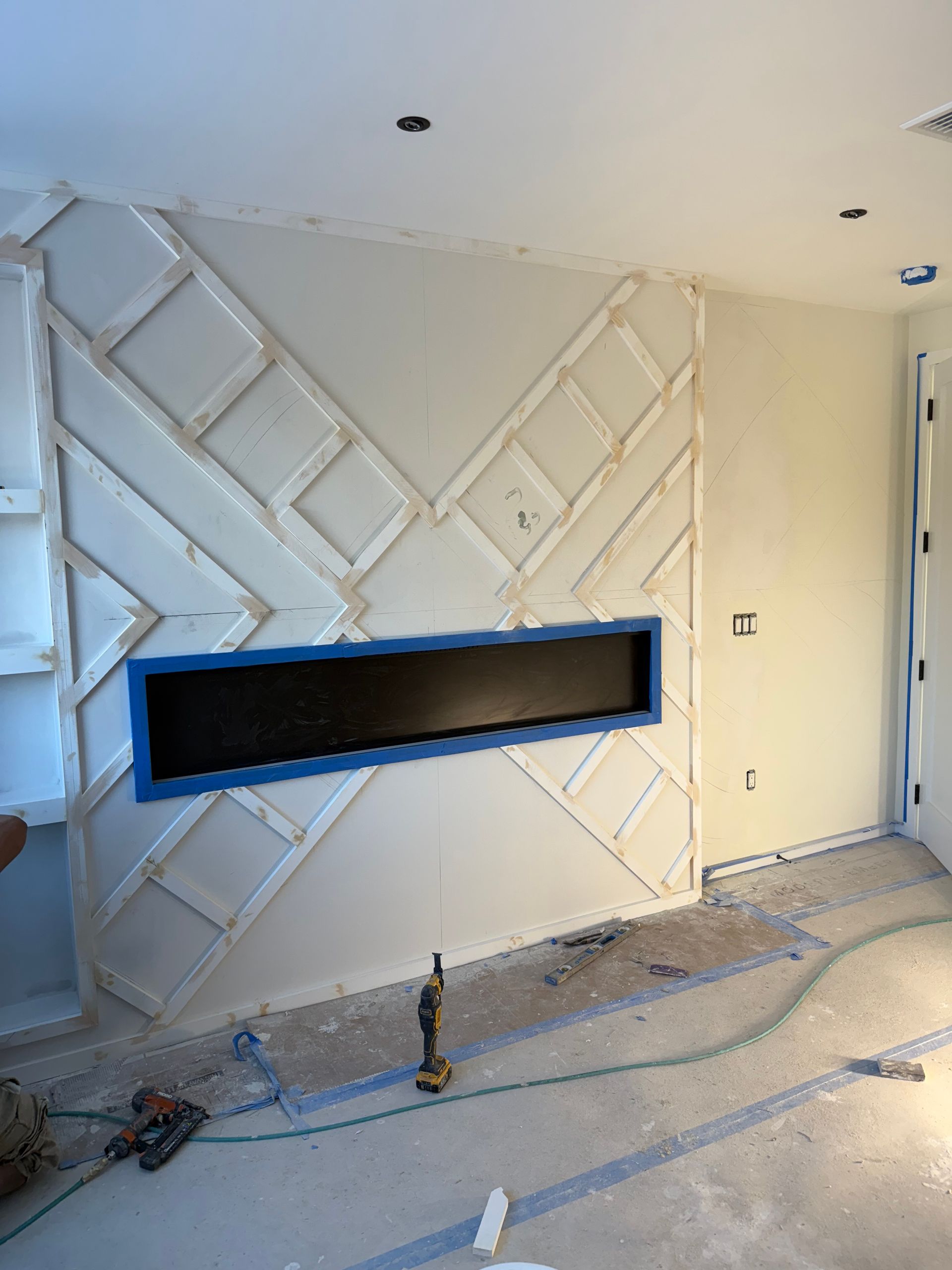 Fireplace with geometric design, unpainted. Blue tape outlines a black rectangular opening.