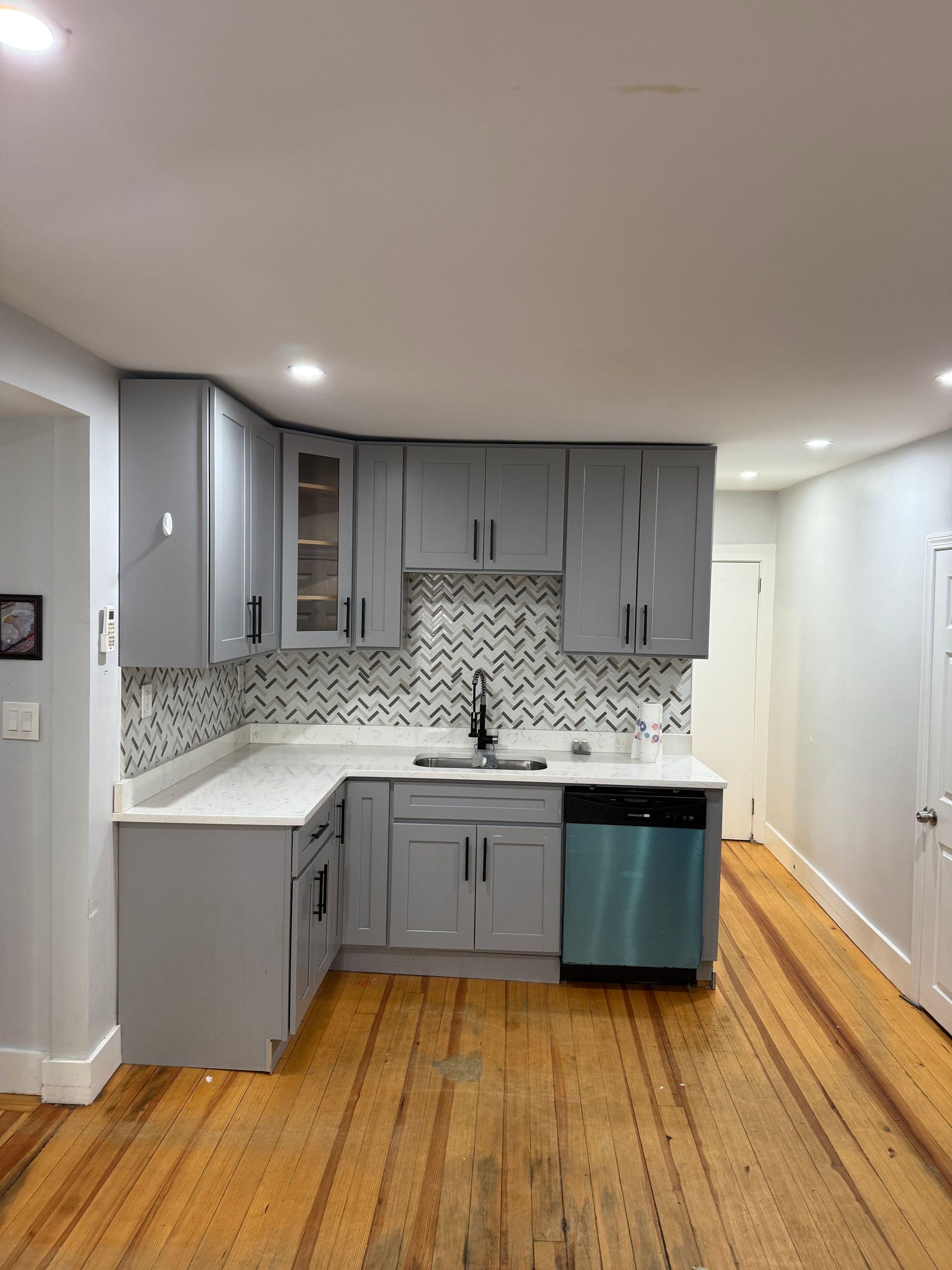 Grey kitchen with light countertops, black fixtures, and stainless steel dishwasher on wooden floors.