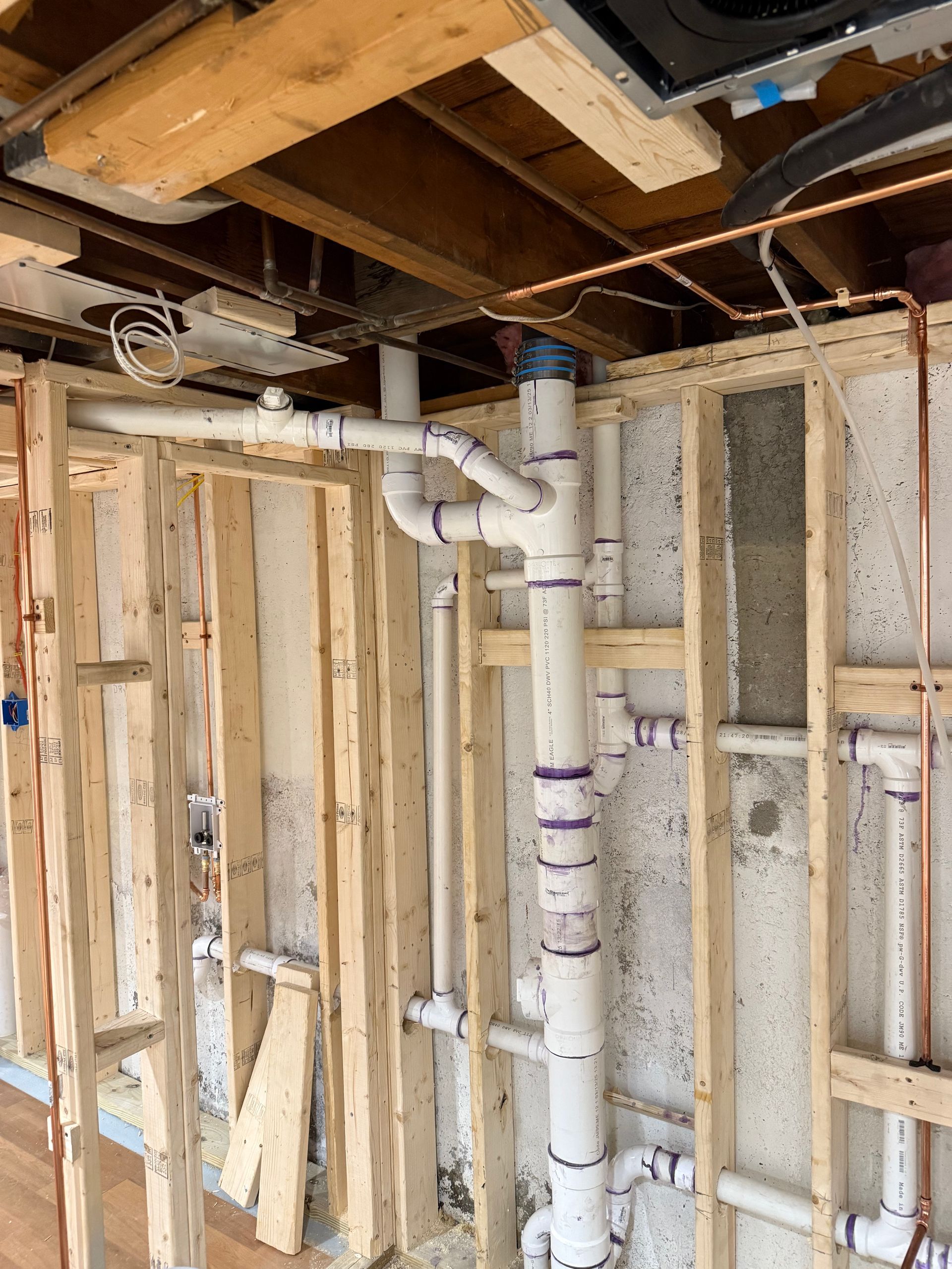 Plumbing pipes installed in a wooden wall, with copper tubing and wiring visible.