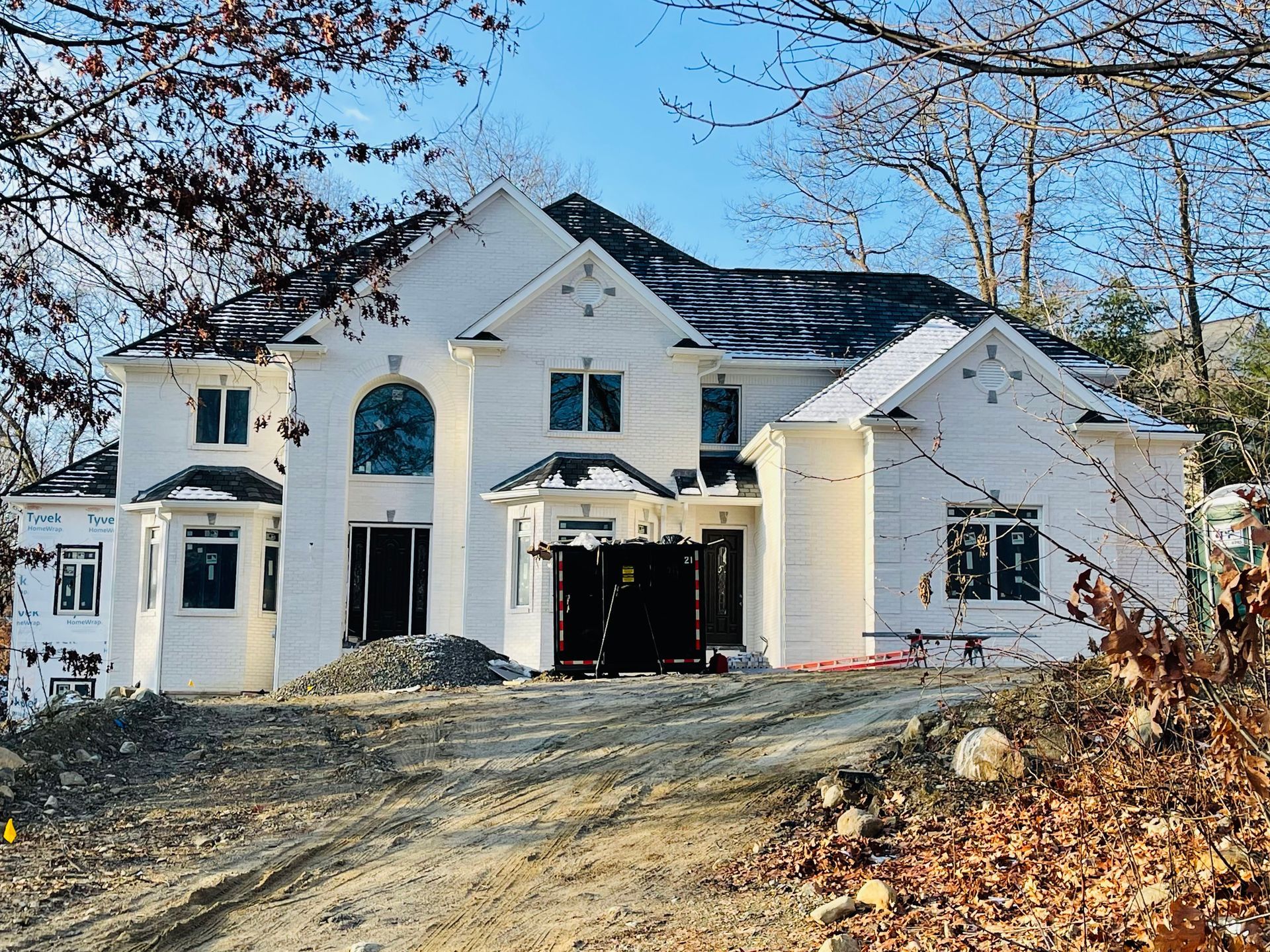 White two-story house under construction with black roof and dirt in front.