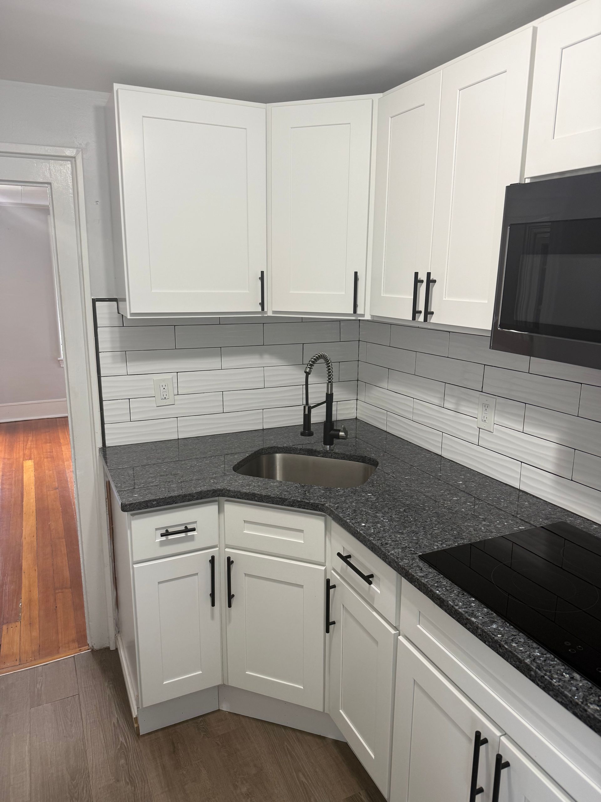 White kitchen cabinets, dark gray countertop, black hardware, stainless steel sink.