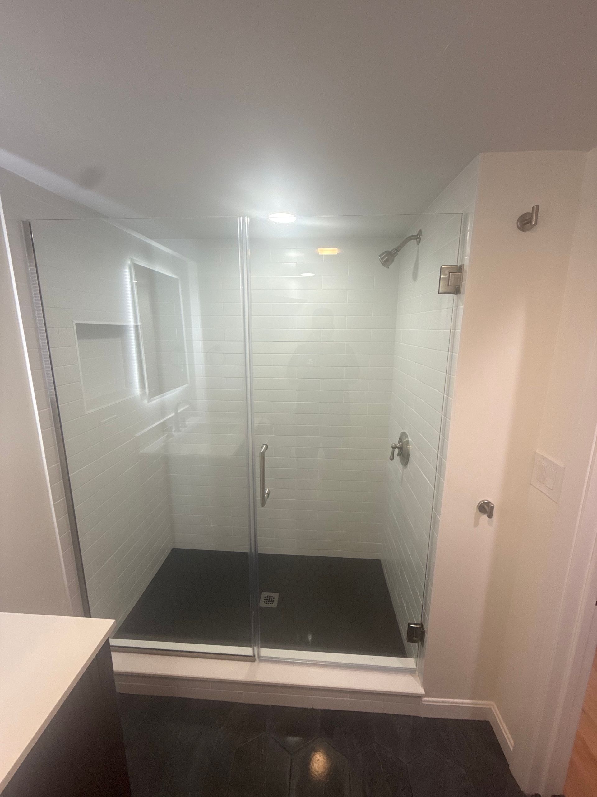 Glass shower enclosure in a tiled bathroom; black floor, white walls.