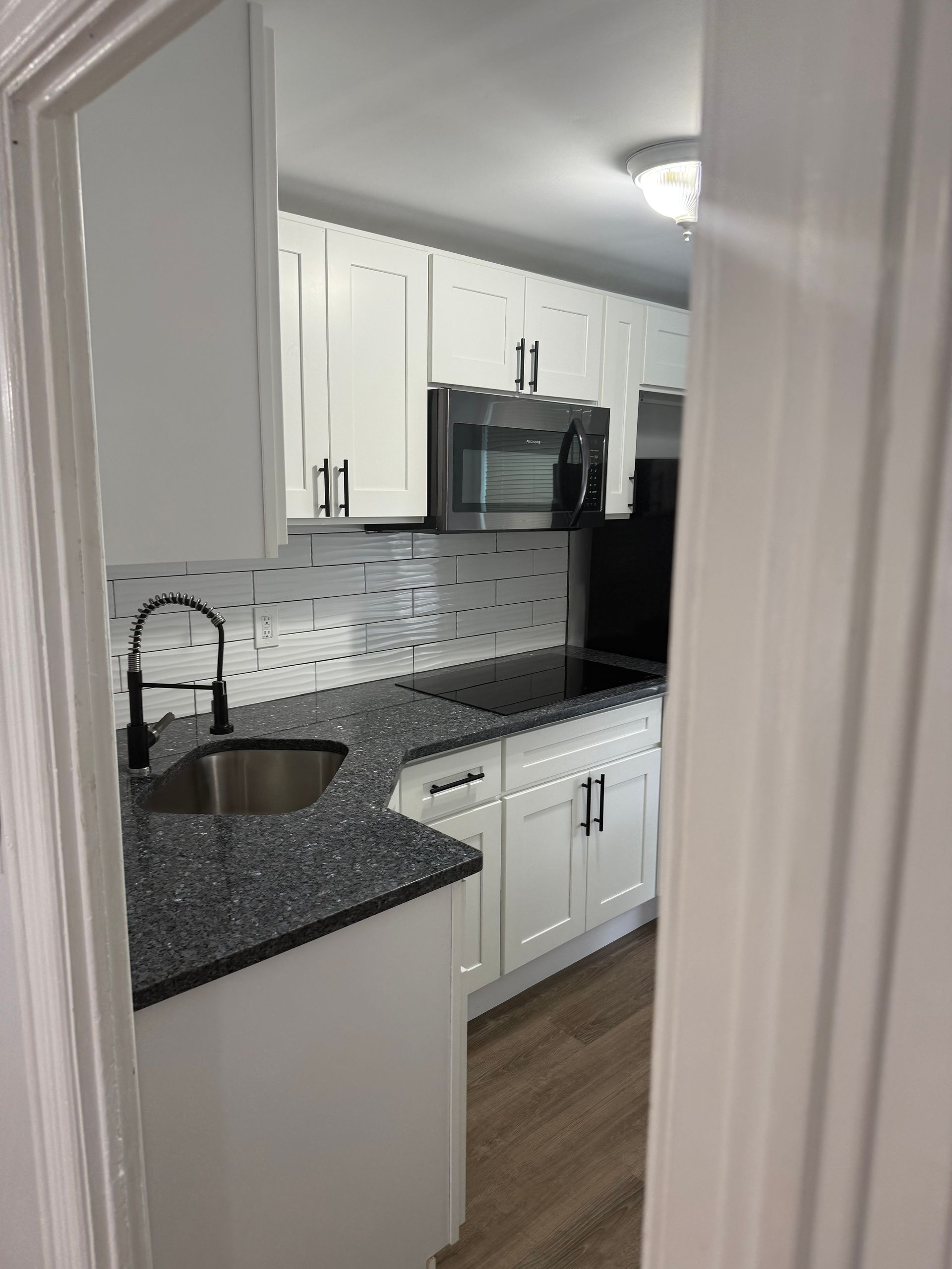 White kitchen with gray countertops and appliances viewed through a doorway.