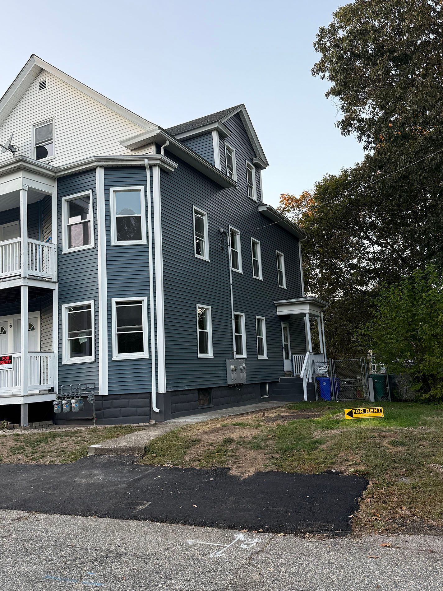Three-story gray house with white trim. Balcony on the left. Driveway in front, grass and trees to the right.