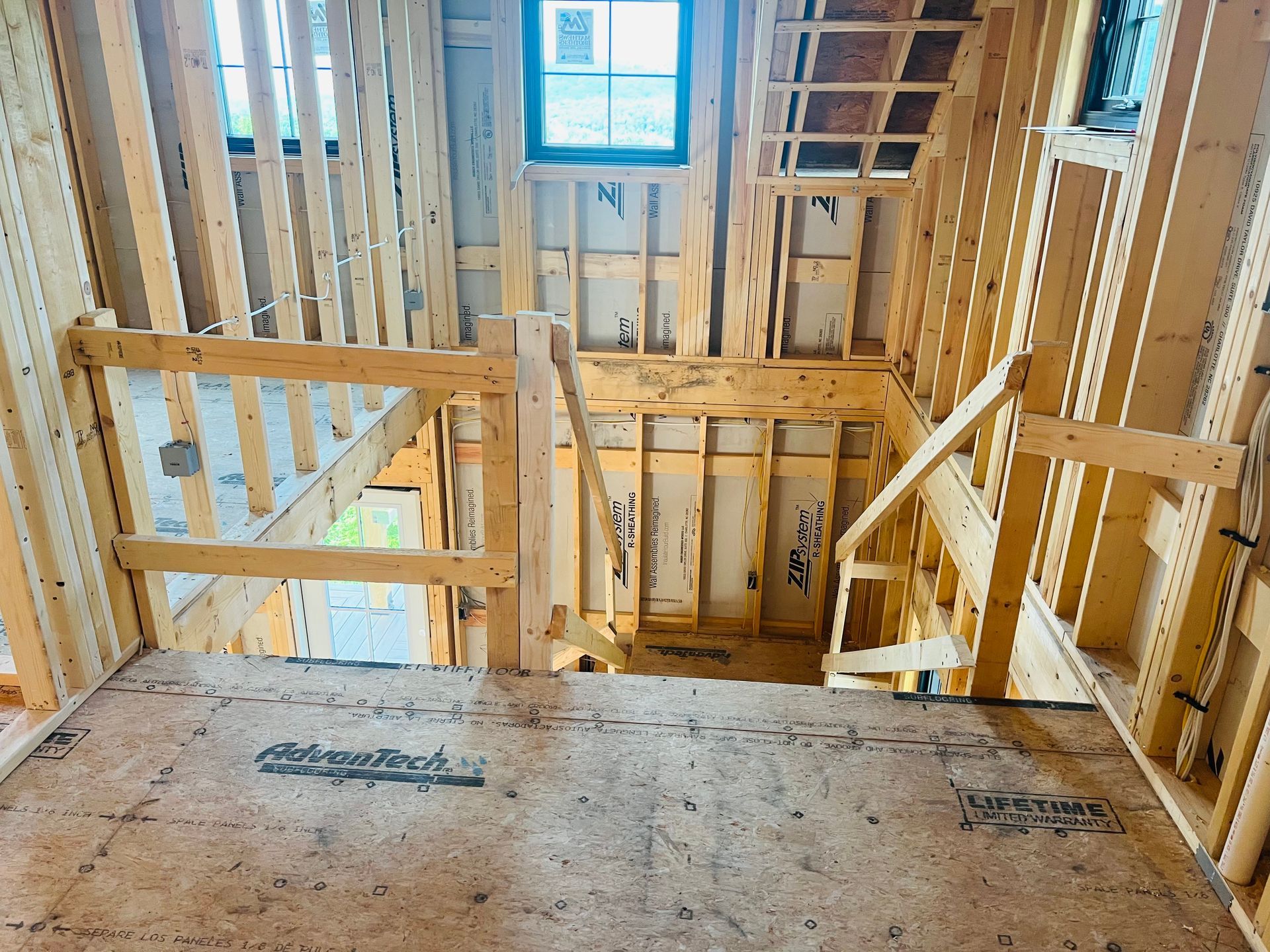 Interior view of a wooden house under construction; staircase, window, and exposed framing.