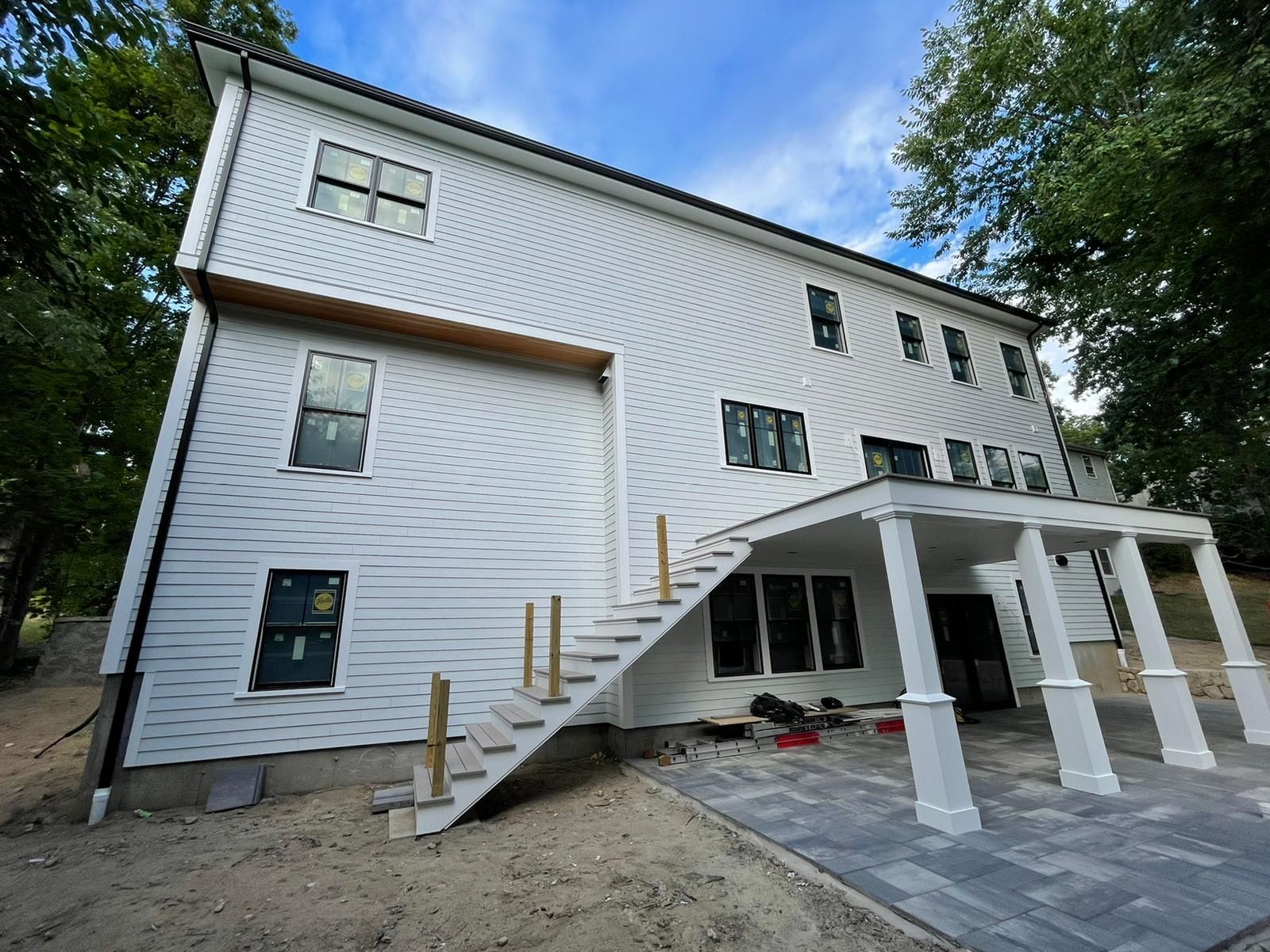 White multi-story house with unfinished stairs and a covered porch with pillars.