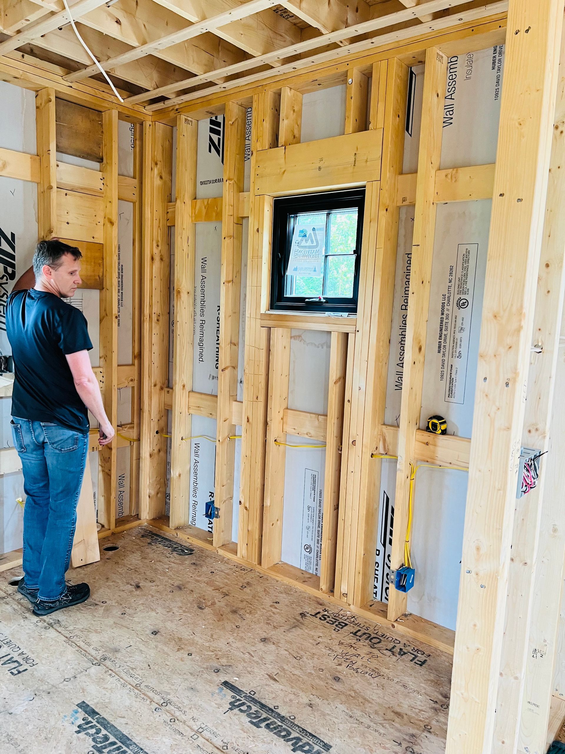 A person inside a room under construction, inspecting wooden wall framing with a small window.