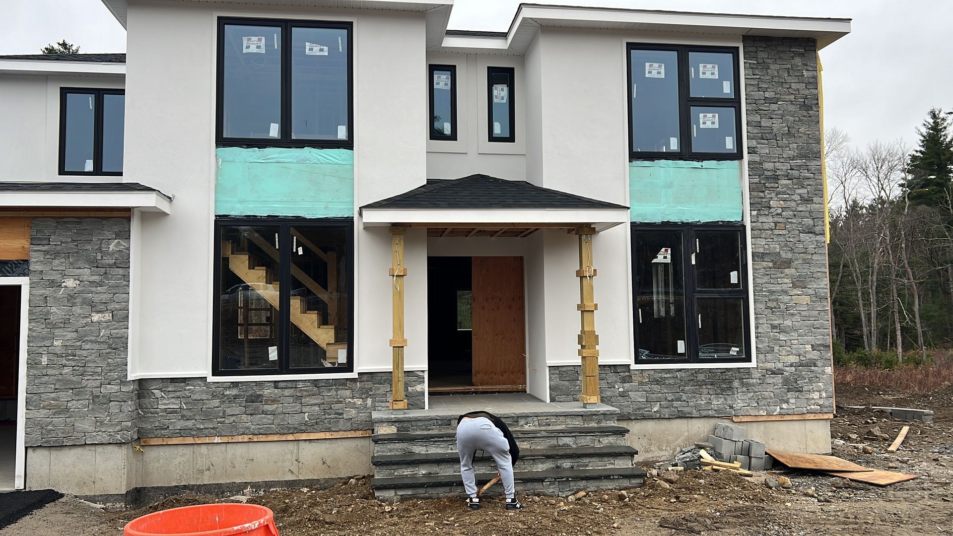 A house under construction with stone accents, dark windows, and a person near the entrance.