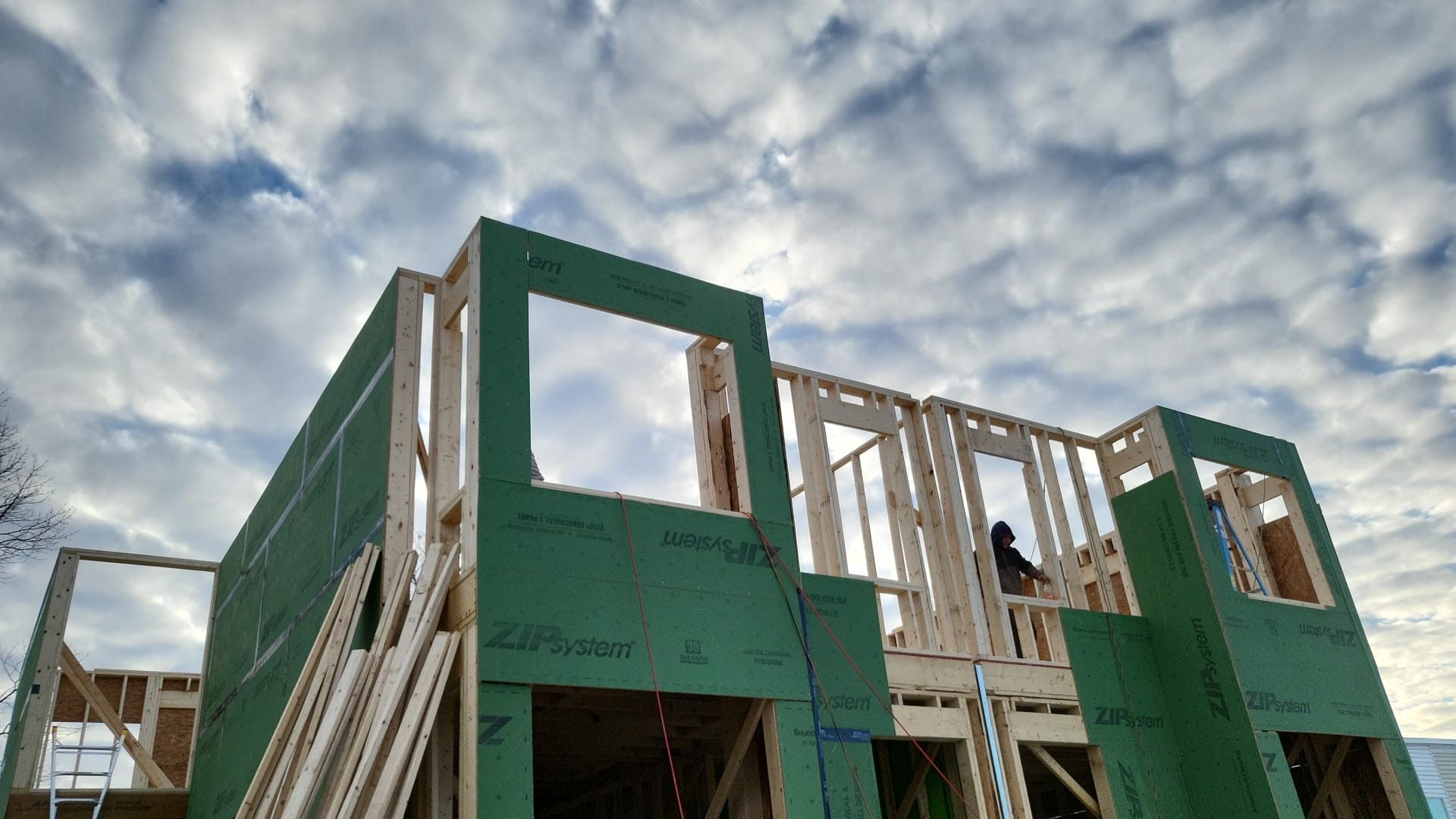 Construction of a new building, framing of walls and windows, cloudy sky in background.
