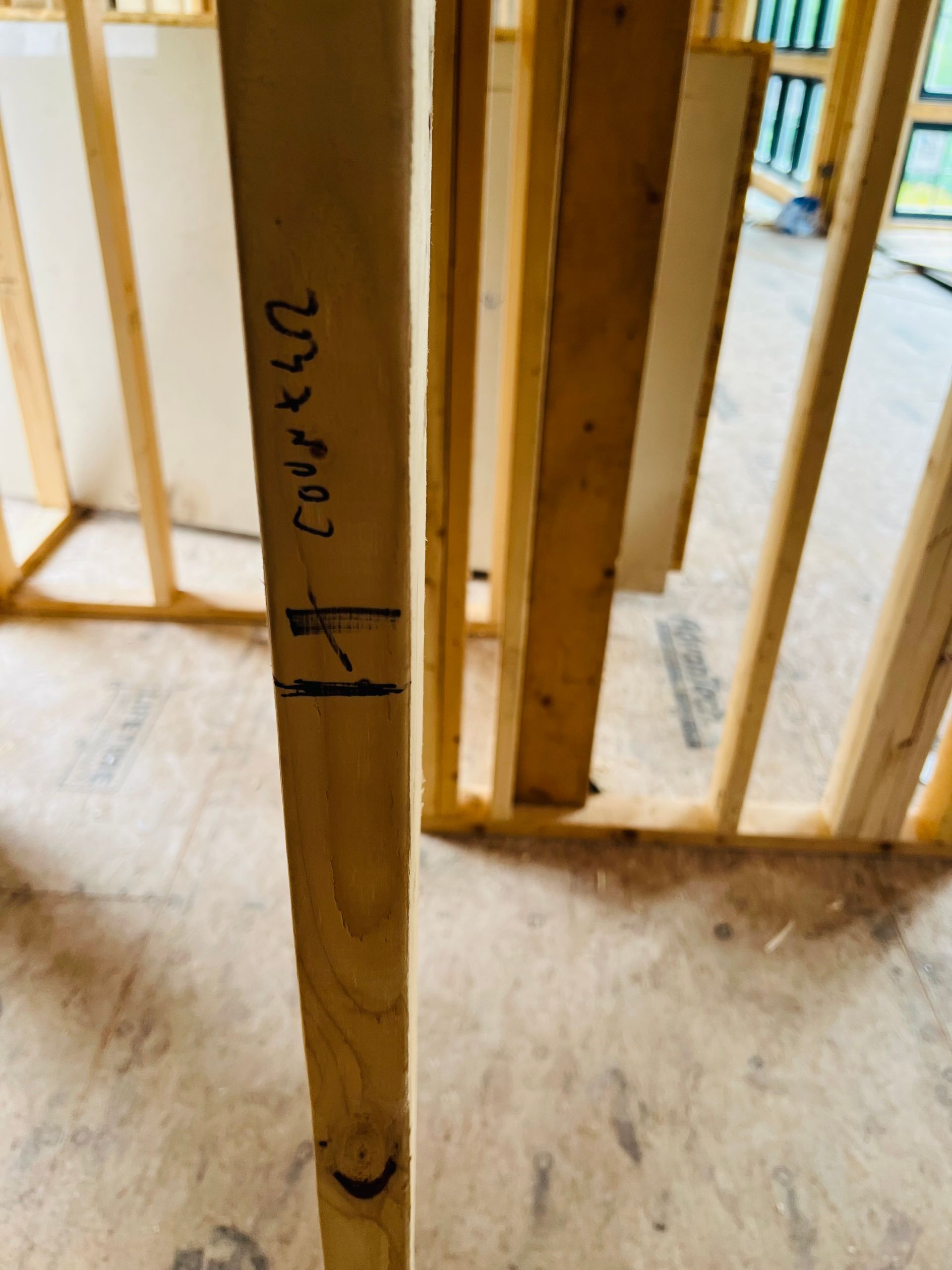Wooden wall studs marked with vertical lines and text, in a wood-framed structure under construction.