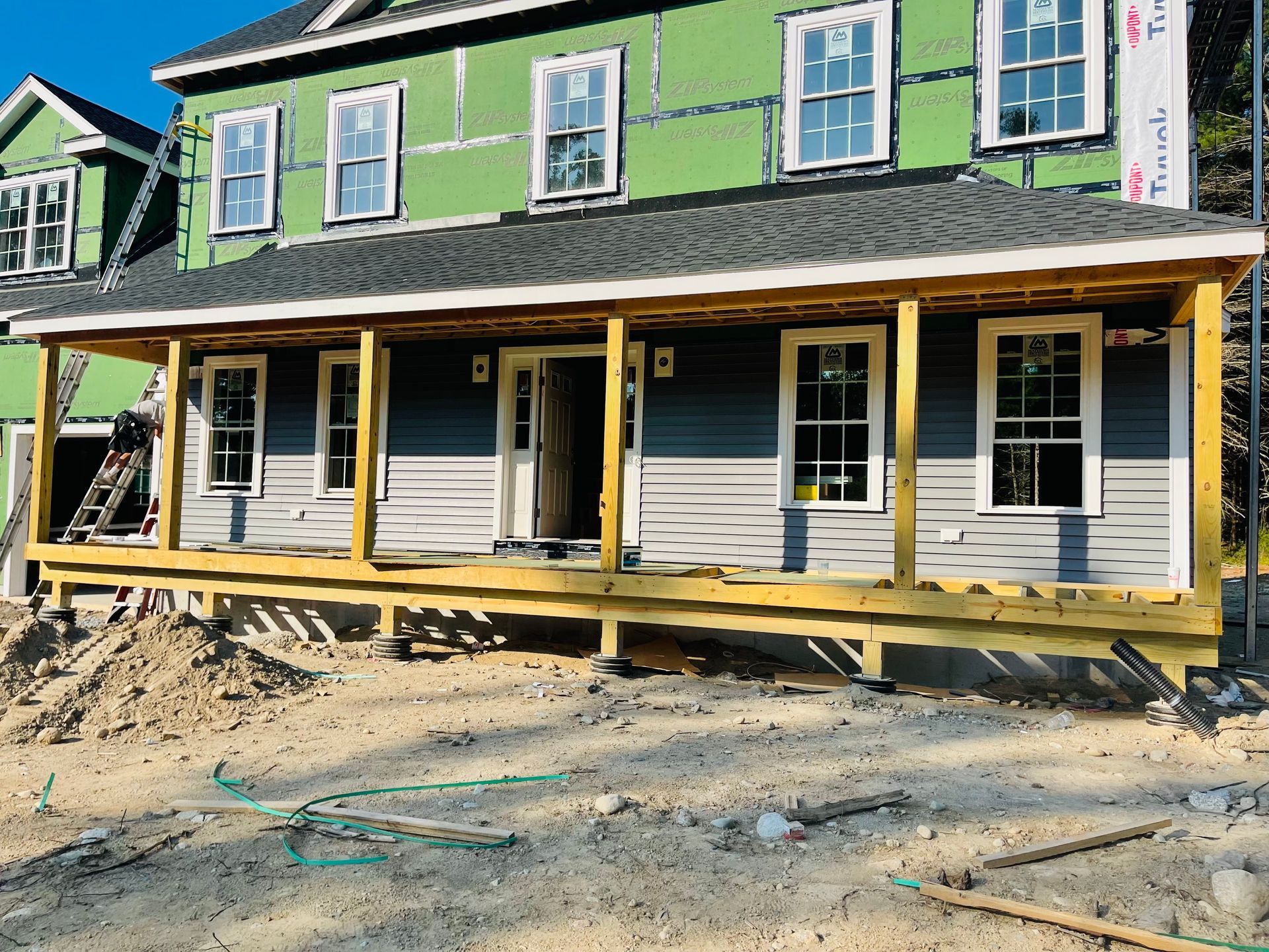 New house under construction, with gray siding, a porch, and several windows.