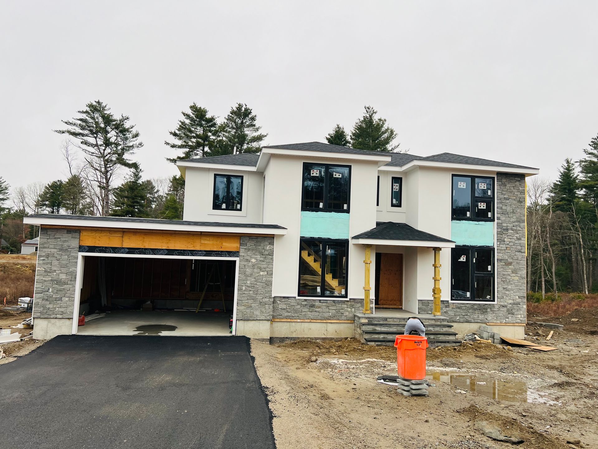 New two-story house under construction with a stone facade, black-framed windows, and asphalt driveway.