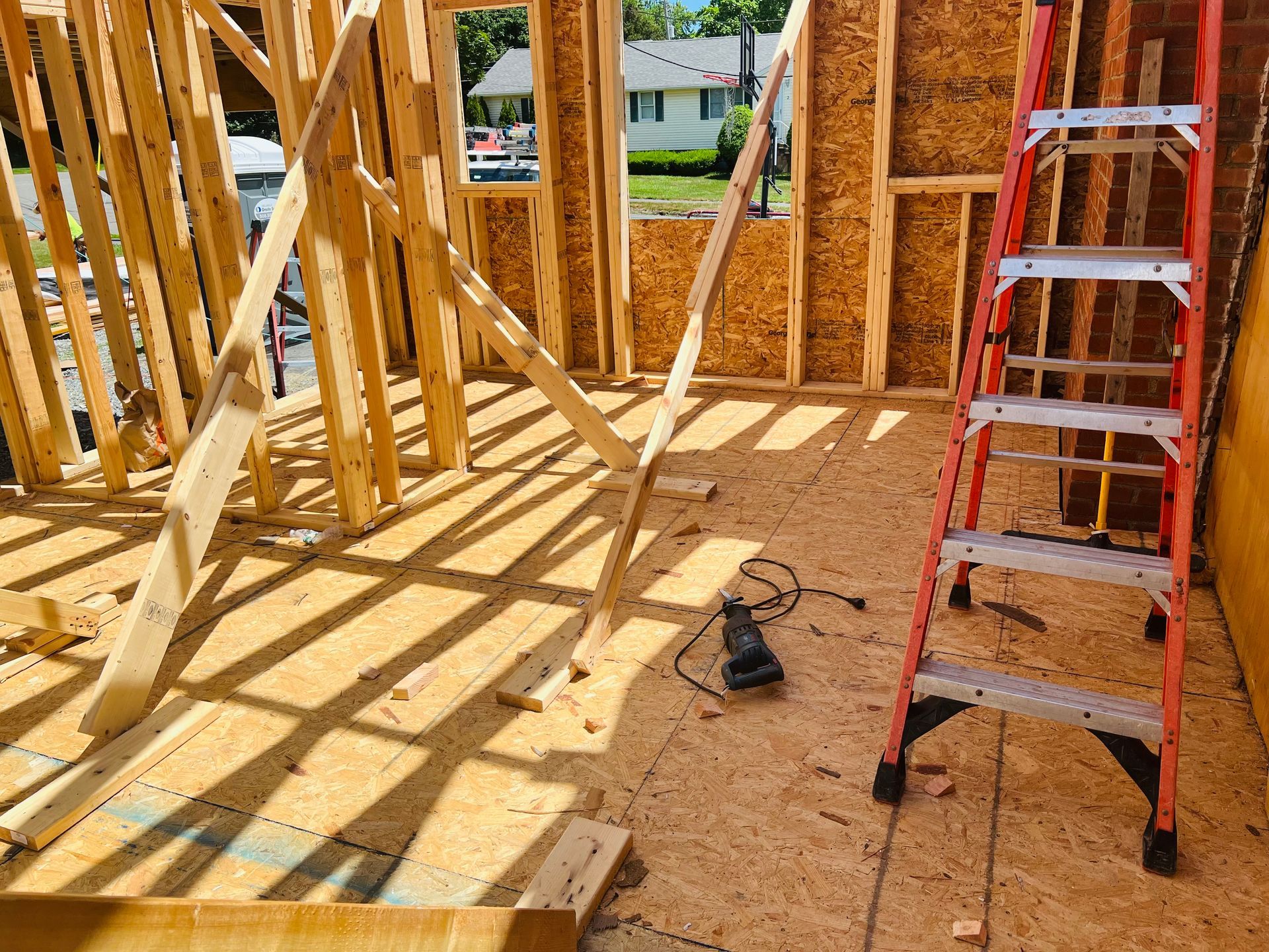 Interior construction of a building with wooden framing, a red ladder, and a power tool.