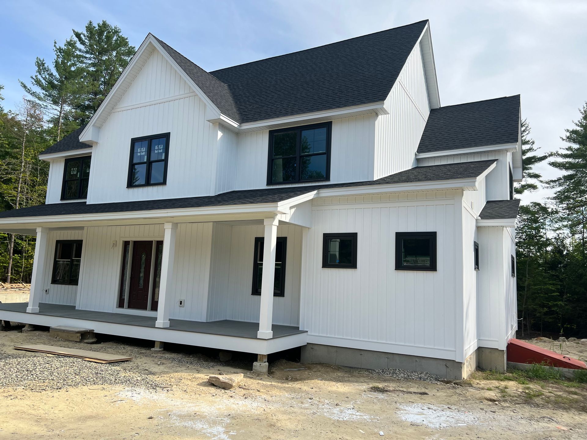 White farmhouse with black windows and roof, porch with pillars.